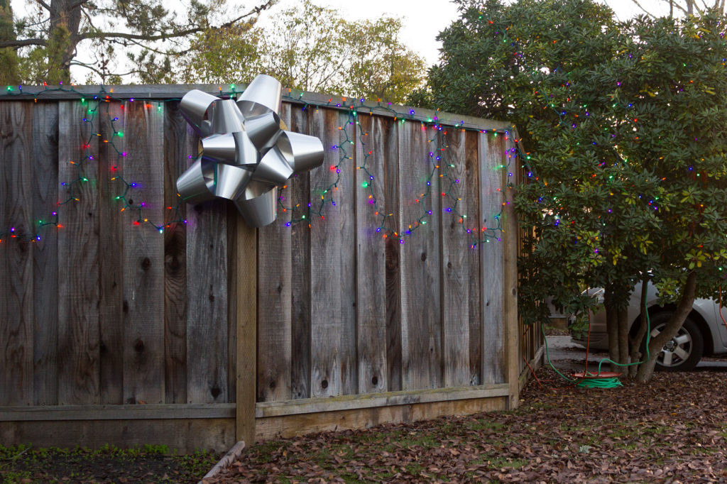 giant metal bow hanging on wood fence with holiday lights
