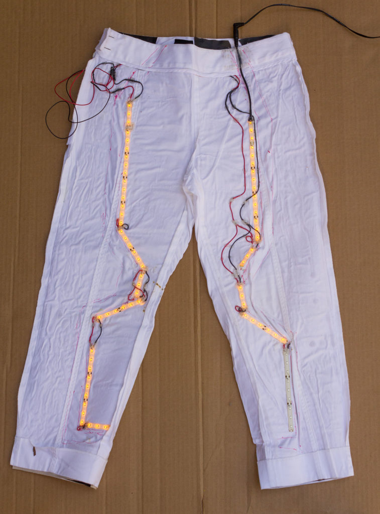glowing amber LED strips laid out in a sci-fi pattern inside white pants